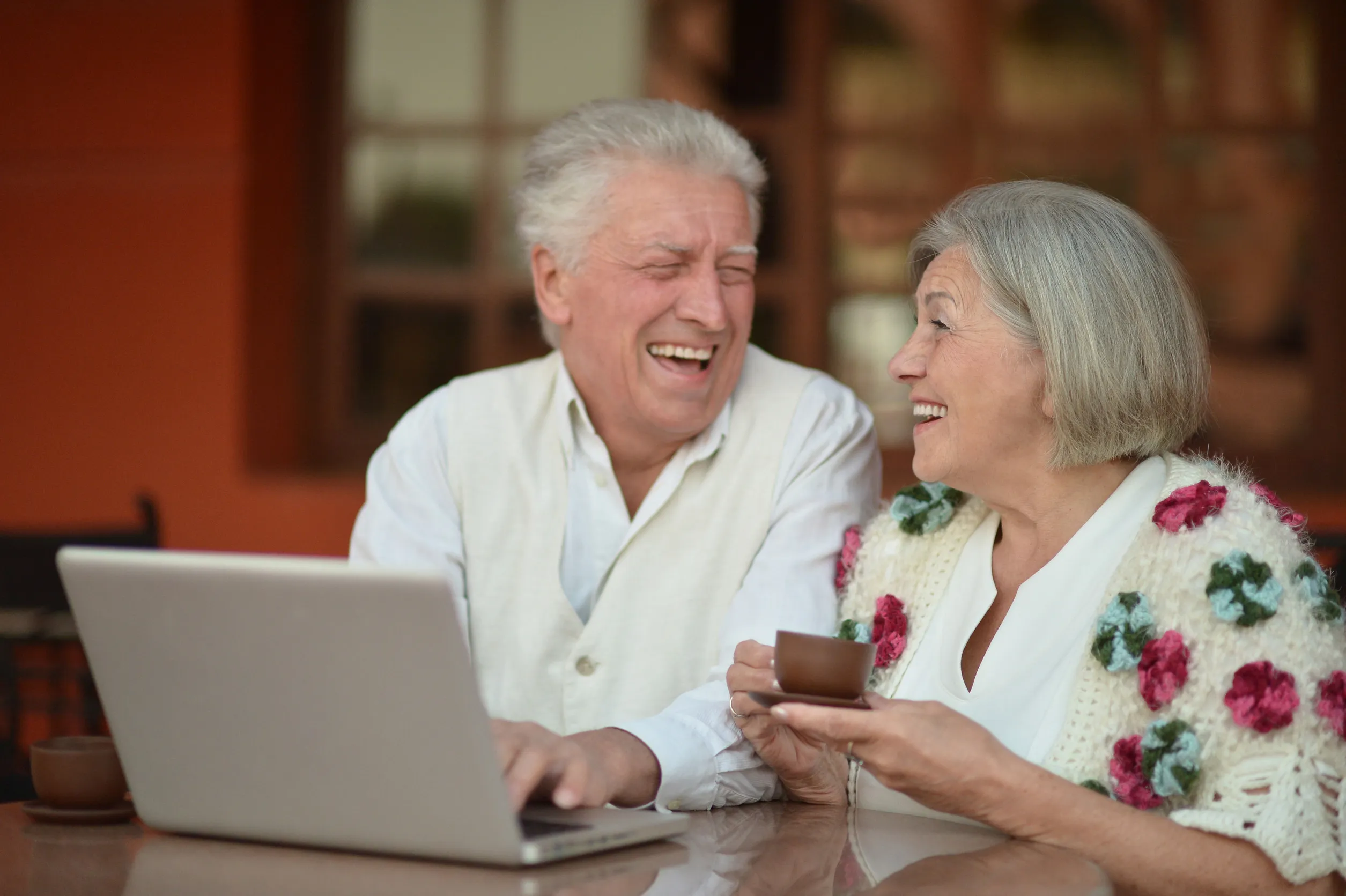 Mature couple sitting with laptop and coffee in hotel